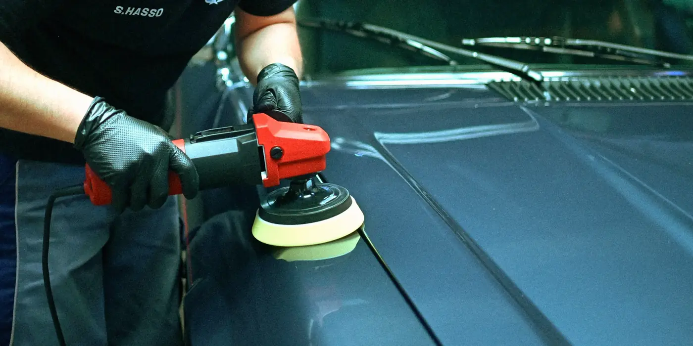 Person polishing a car hood with an orbital buffer