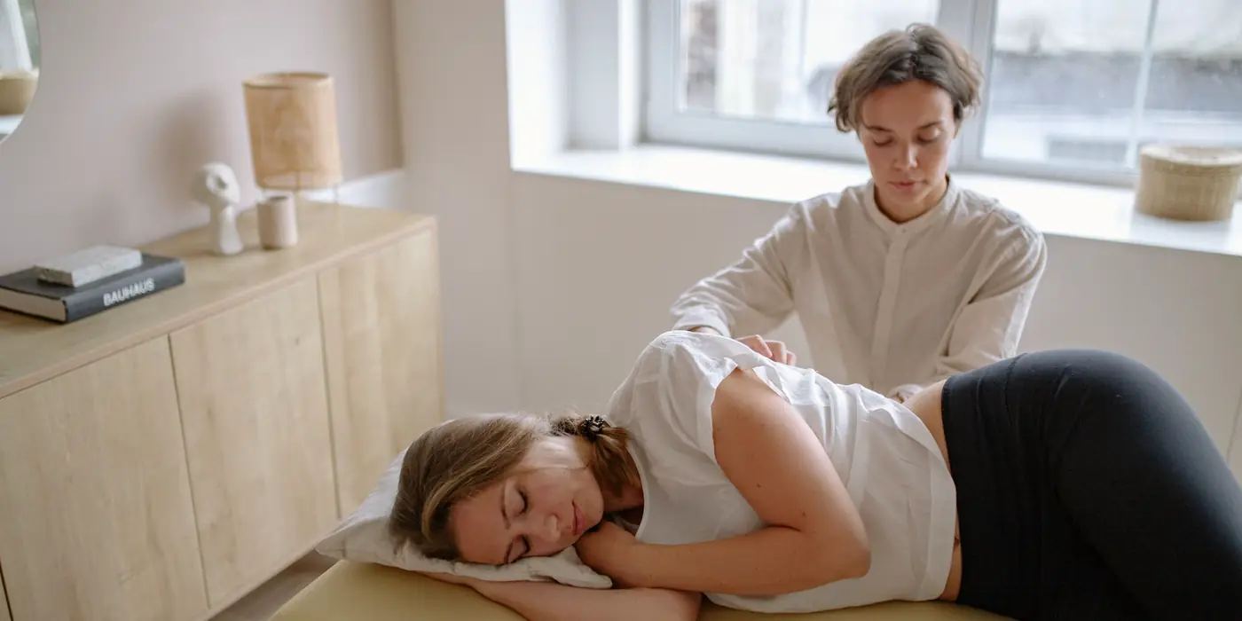 Practitioner giving hands-on treatment to a relaxed patient on a treatment table in a bright room