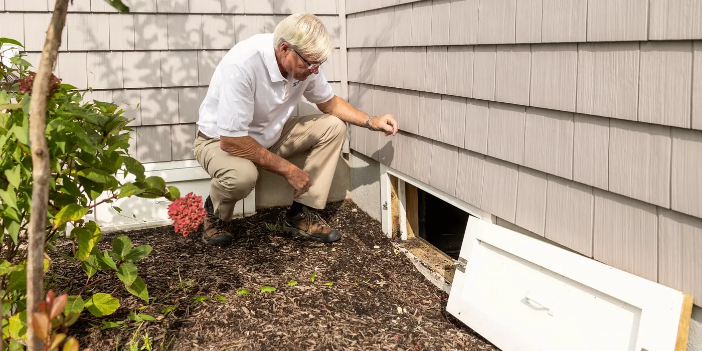 Inspector kneeling at a crawl space opening on the side of a house
