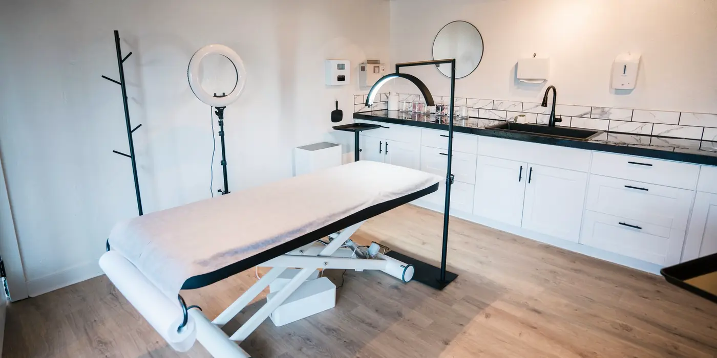 Modern aesthetic treatment room with a treatment table, ring light and white cabinetry